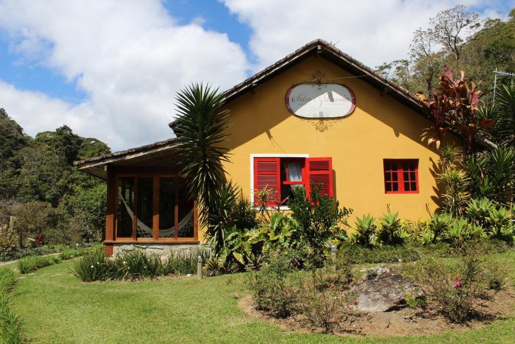 Fachada da pousada Sitio e Poesia em Teresópolis com paredes amarelas, janelas vermelhas e bastante árvores em volta.