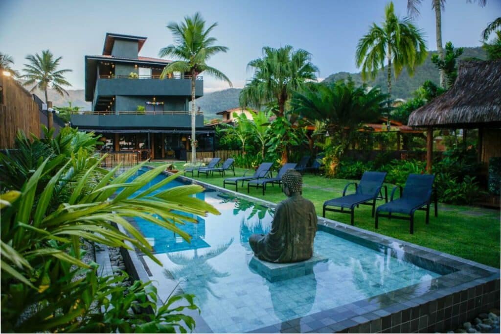 Piscina da Pousada TeMoana com um gramado ao redor e espreguiçadeiras azuis, além de muitas árvores