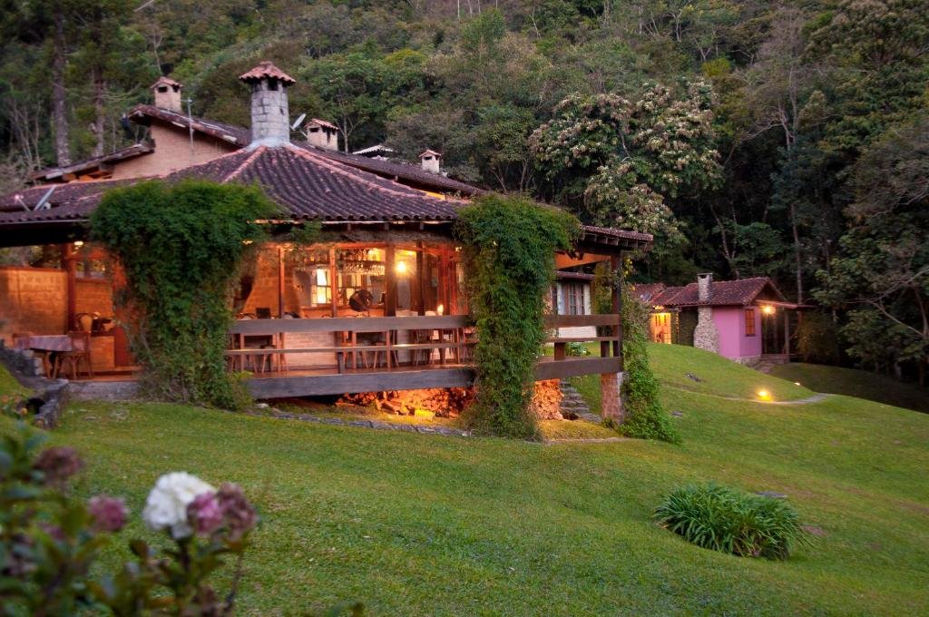 Espaço redondo iluminado com mesas e grande área de gramado verde e árvores em volta, ilustrando post pousadas em Visconde de Mauá.
