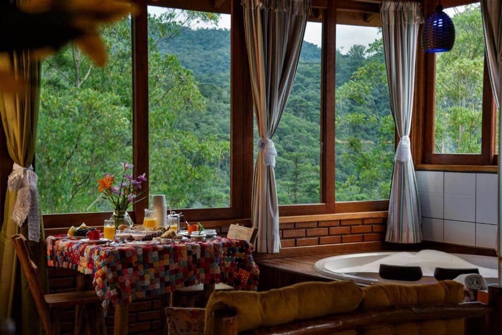 Mesa com comidas em cima perto de uma grande janela de vidro com vista para as árvores durante o dia, ilustrando post pousadas em Visconde de Mauá.
