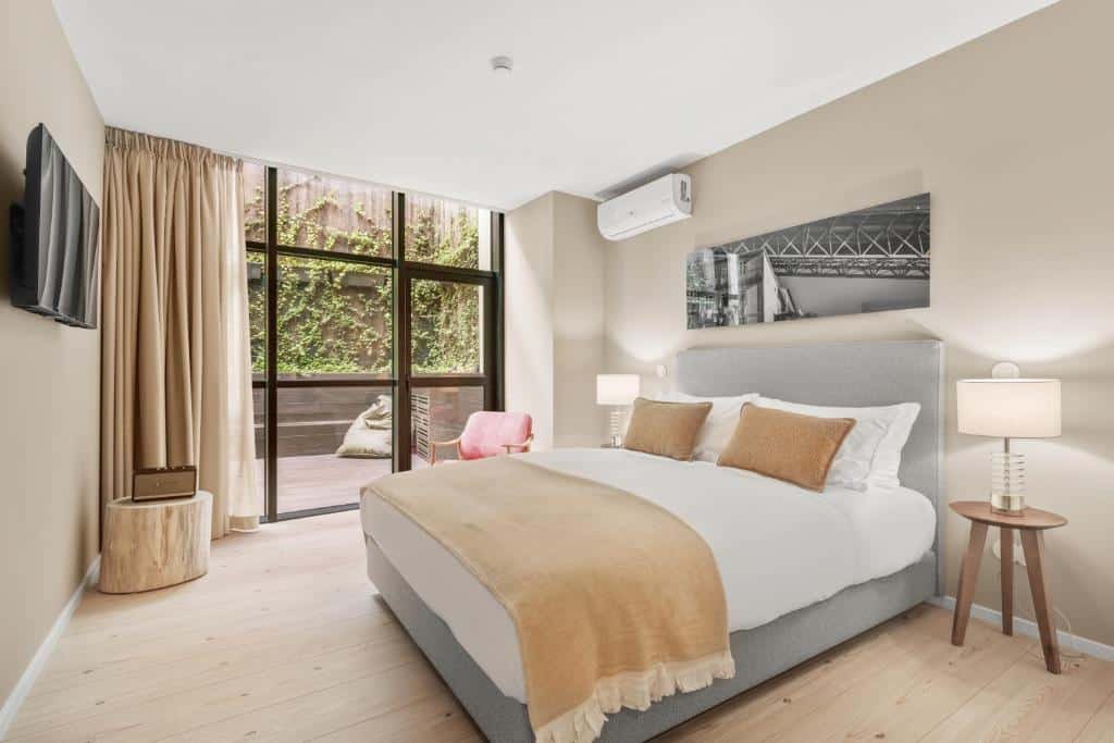 Quarto do 108MM House com cama de casal do lado direito da imagem, dos dois lados da cama duas luminárias e em frente a cama uma TV presa na parede. Representa melhores hotéis no Porto.