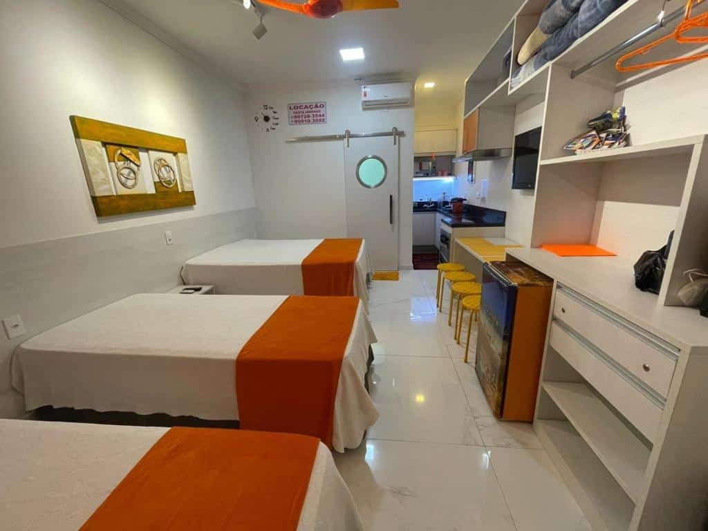 Acomodação do Amarilis, duas camas de casal, uma pequena cozinha, um ar-condicionado, um armário de conceito aberto, uma bancada com quatro lugares, um frigobar e uma televisão, para representar pousadas em Riviera de São Lourenço