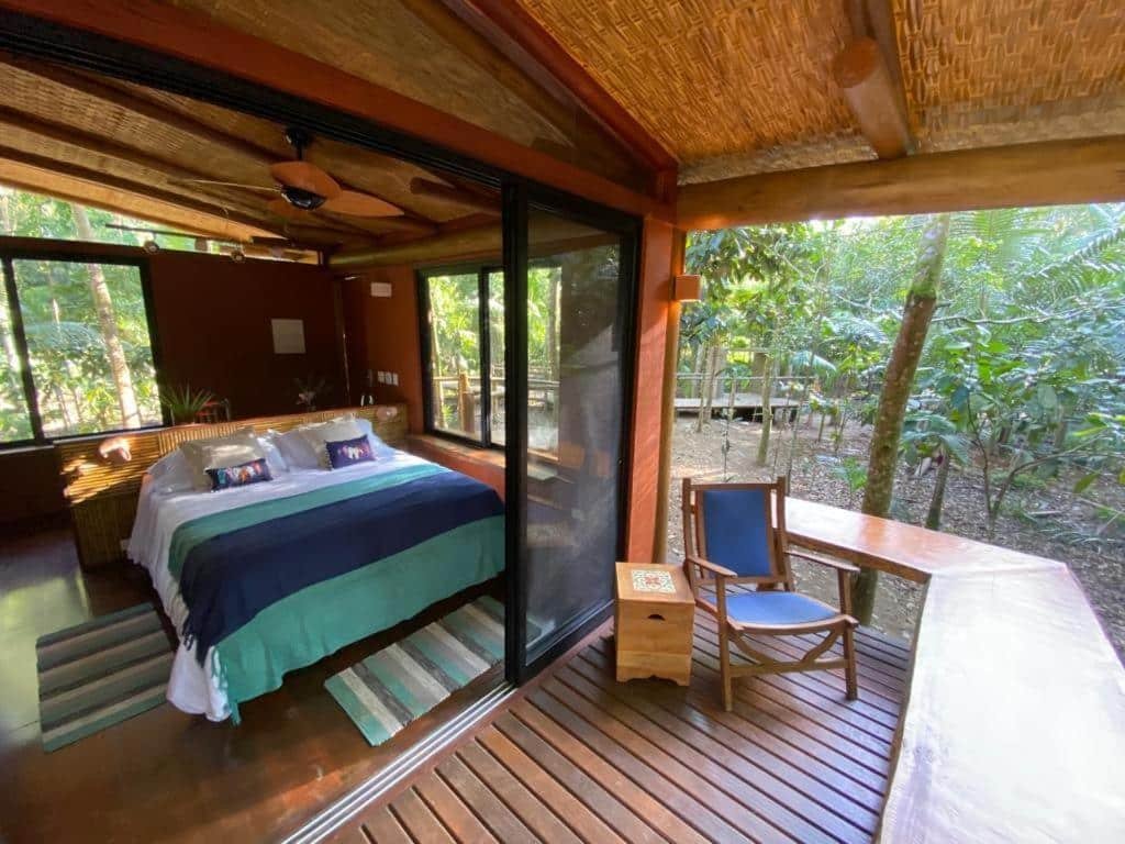 Quarto no Banana Bamboo Ecolodge com varanda térrea virada para a natureza, uma cama de casal, tudo em madeira e com janelas de vidro, para representar resorts em Ubatuba