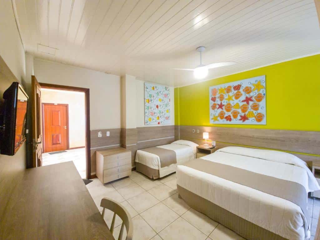 Quarto no Beach Hotel Maresias com uma cama de casal e uma de solteiro, uma mesa de escritório com uma cadeira, além de uma televisão e um ventilador de teto