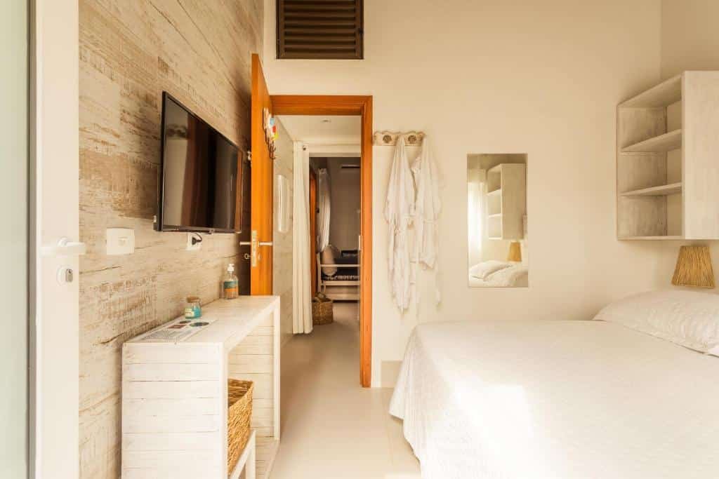 Quarto da Casa d’Aroeira Condomínio Residencial Luxo com cama de casal do lado direito da imagem e em frente a cama uma cômoda e em cima preso na parede uma TV pendurada.