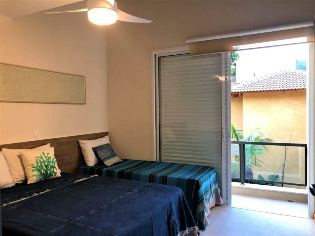 Quarto da Casa na praia linda de Juquehy com cama de casal do lado direito da imagem no canto e do lado esquerdo da cama uma cama de solteiro.