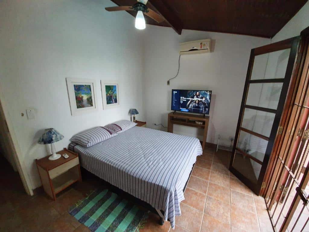 Quarto da Casa pé na areia em Toque Toque, uma cama de casal, dois abajures, uma sacada de frente para cama, uma televisão sob um móvel e um ar-condicionado