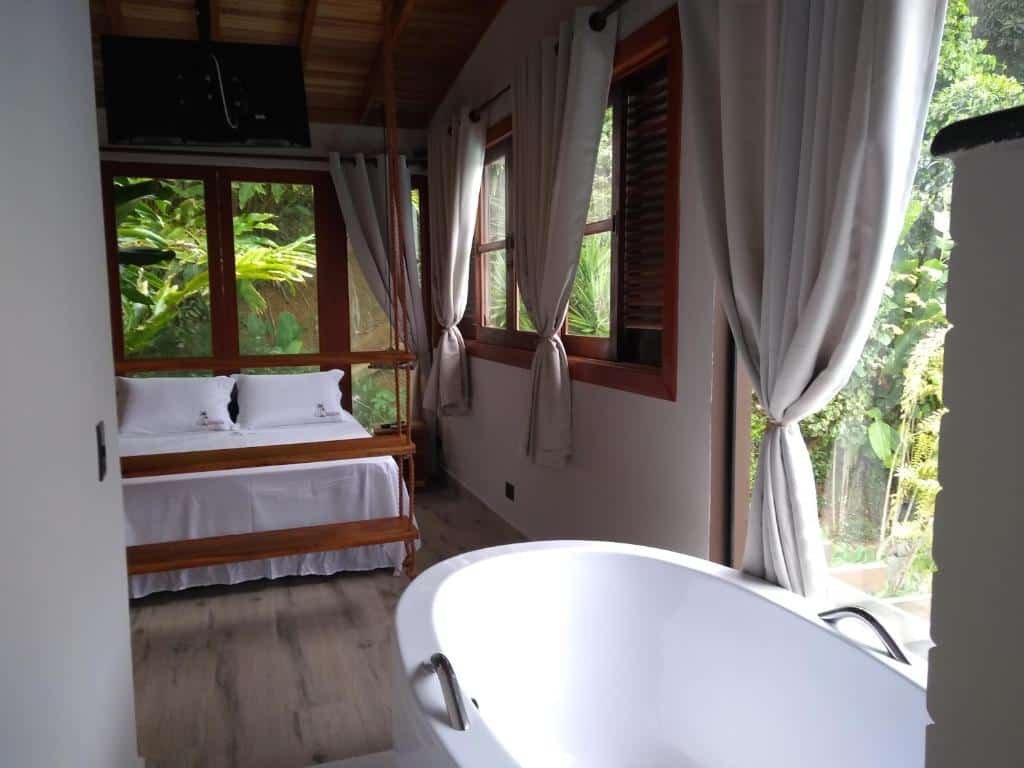 Quarto no El Shadday Pousada Boutique com uma cama de casal, uma ampla porta de vidro que leva para o jardim, e há uma banheira no canto direito do quarto, para representar resorts em Ubatuba