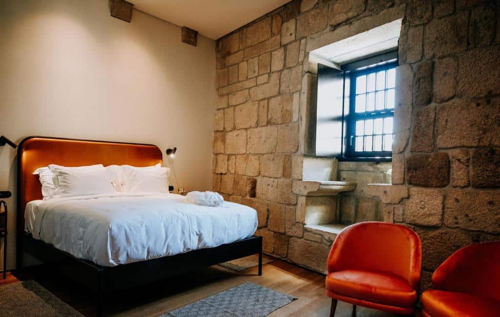 Quarto do Exmo Hotel by Olivia com cama de casal do esquerdo e em frente a cama com duas poltronas.