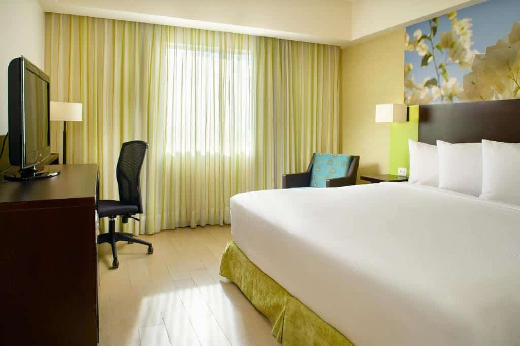 Quarto do Fairfield Inn Los Cabos com cama de casal ampla, poltrona ao lado esquerdo, TV a frente da cama em cima de uma cômoda com mesa de trabalho. 
