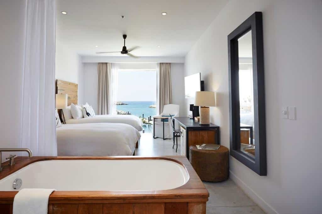 Quarto do Hotel El Ganzo Adults Only com banheira de hidromassagem, duas camas de solteiro, TV em frente a cama com mesa de trabalho e sacada com vista para o mar.