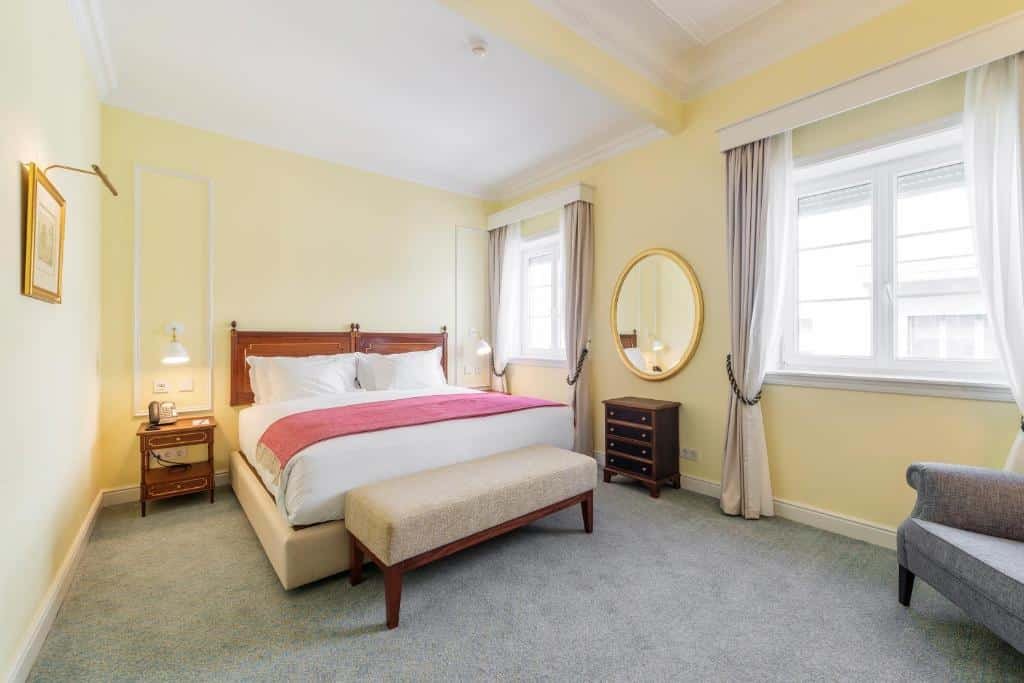Quarto do Hospes Infante Sagres Porto com cama de casal do lado esquerdo, uma poltrona no pé da cama e a frente uma poltrona. Representa hotéis românticos no Porto.