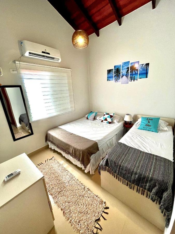 Quarto do Linda casa em Juquehy a 150 metros da praia com uma cama de casal do lado esquerdo da imagem a frente, do lado esquerdo da cama uma cômoda com luminária e do lado esquerdo da cômoda uma cama de solteiro. Representa airbnb na Barra do Sahy.