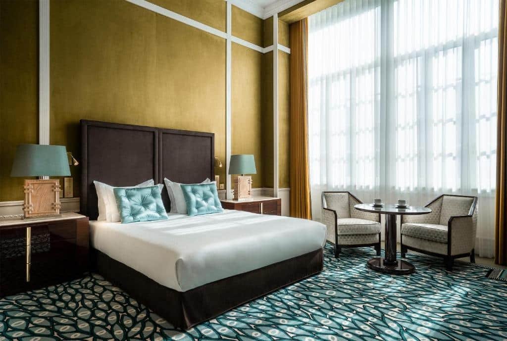 Quarto do Maison Albar Hotels Le Monumental Palace com cama de casal do lado esquerdo e em frente a cama uma cômoda com luminária. Representa melhores hotéis no Porto.