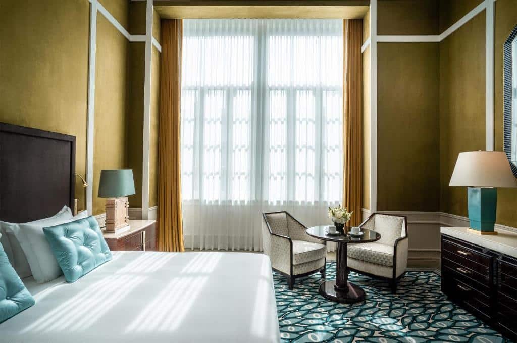 Quarto do Maison Albar Hotels Le Monumental Palace com cama de casal do lado esquerdo e em frente a cama uma cômoda com luminária. Representa hotéis românticos no Porto.