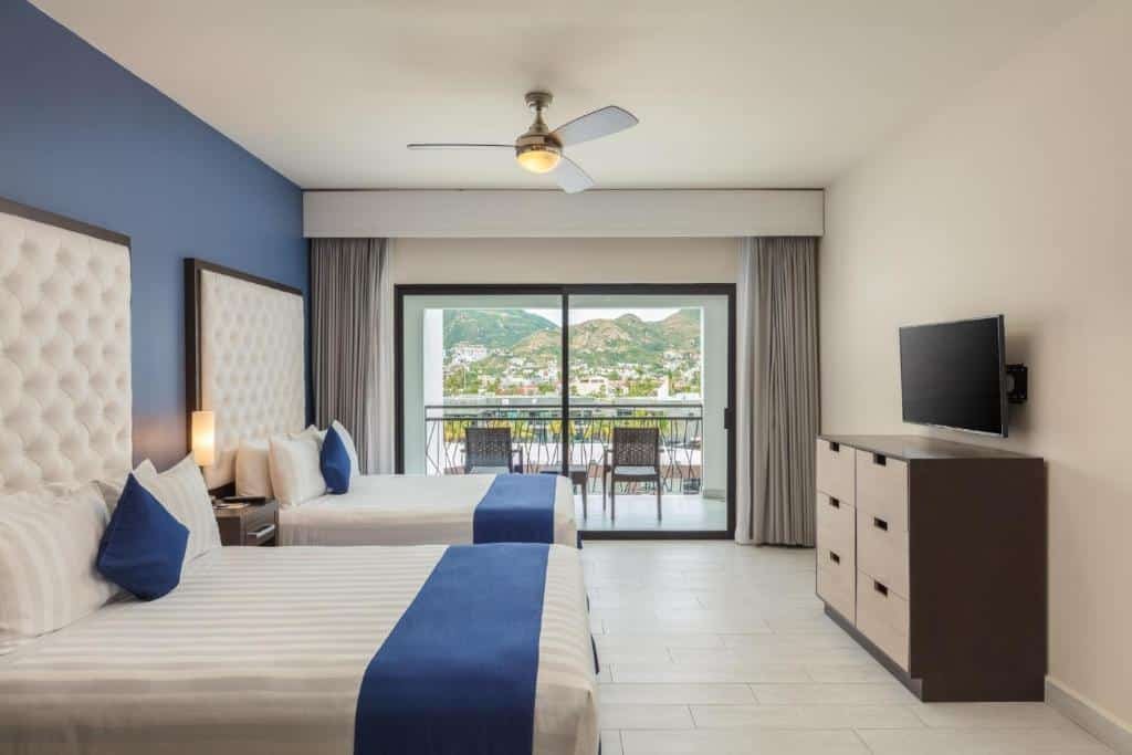 Quarto do Medano Hotel and Suítes com cama de solteiro e uma cômoda do meio. TV em frente a cama com uma cômoda embaixo e sacada com cadeiras.