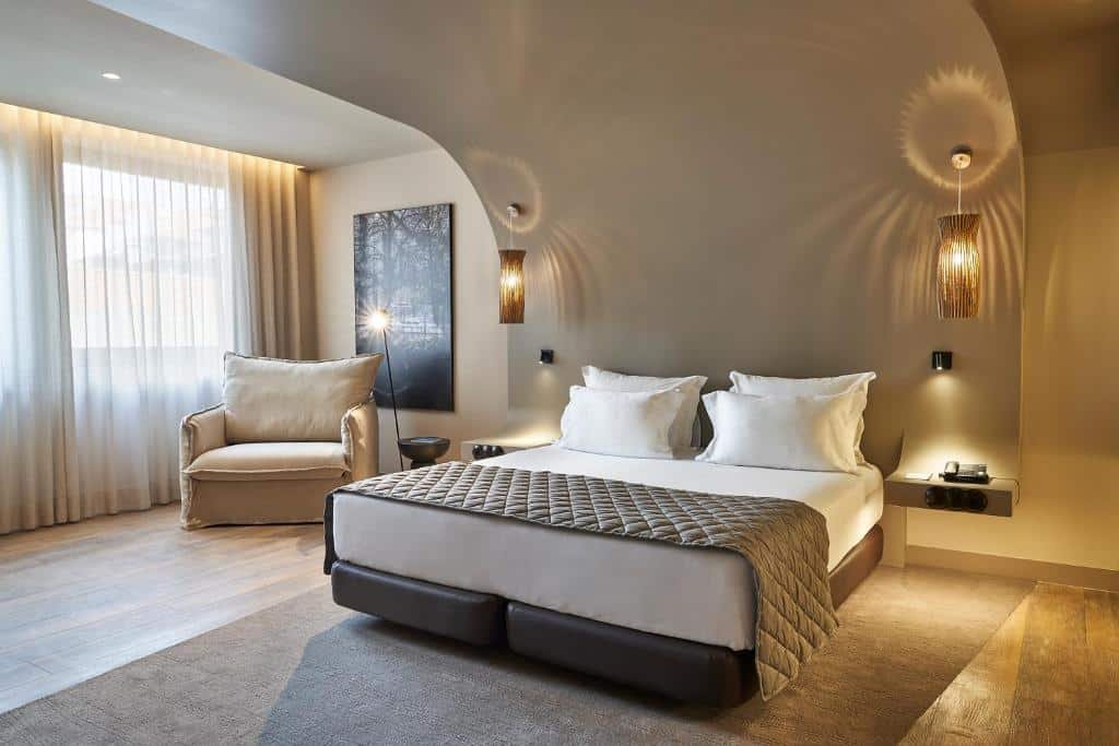 Quarto do PortoBay Teatro com cama de casal do lado direito e do lado esquerdo da cama uma poltrona.