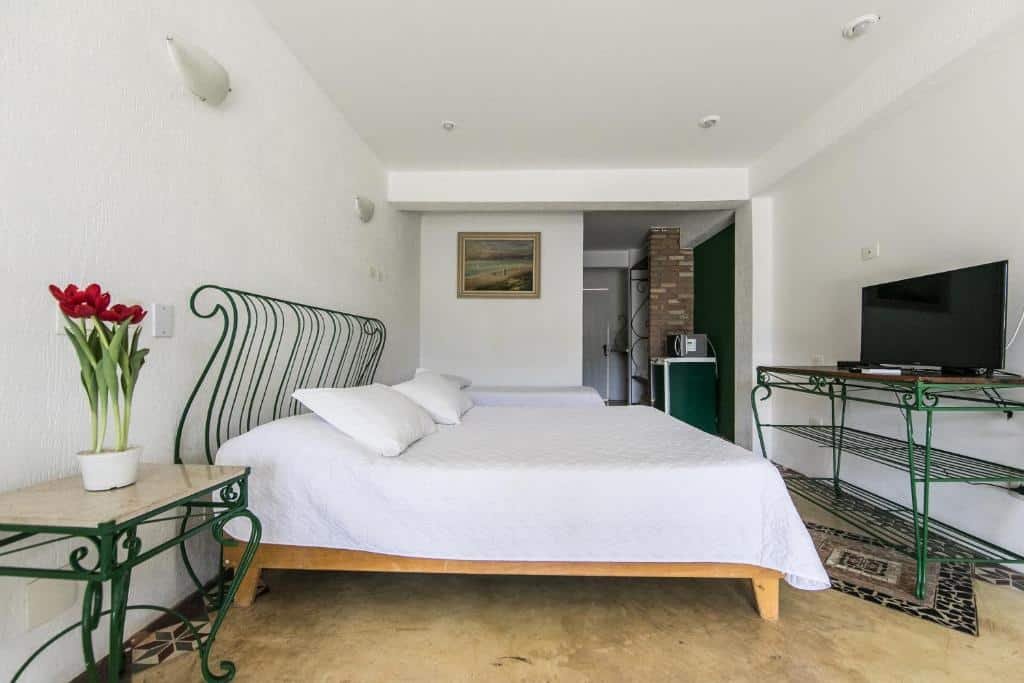 Quarto da Pousada Brig Maresias com uma cama de casal, uma de solteiro, um móvel com uma televisão em cima de frente para a cama, para representar pousadas pé na areia em Maresias