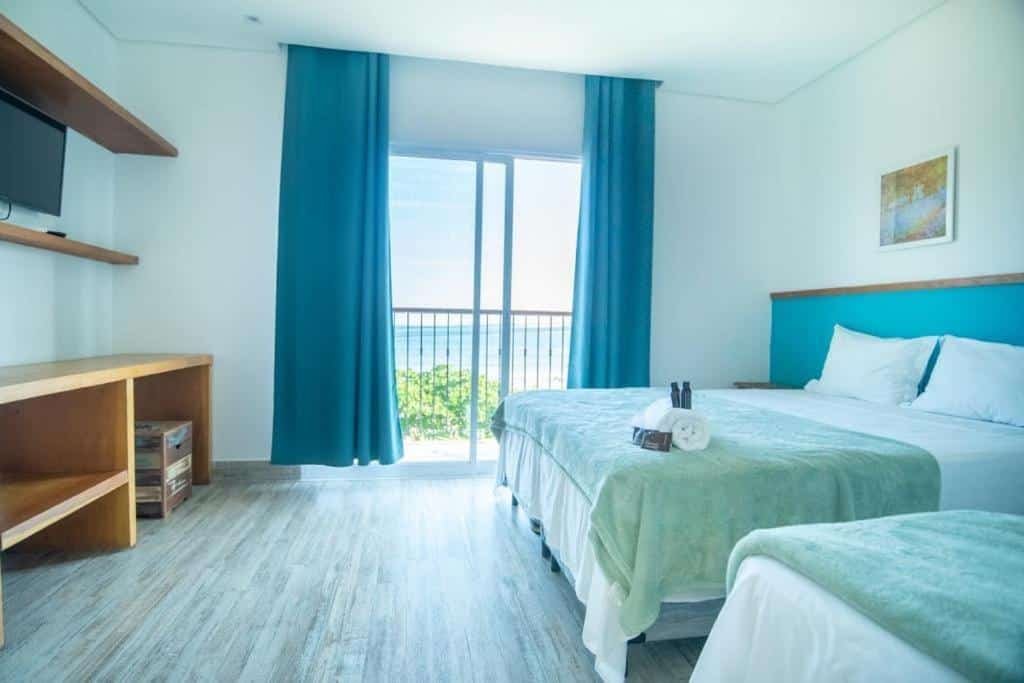 Quarto na Pousada Conca di Mare - Restaurante - Pé na areia com serviço de praia com uma sacada dando vista para a praia, uma televisão, uma cama de casal, uma de solteiro, uma toalha e travesseiros sob a cama, para representar pousadas em Riviera de São Lourenço