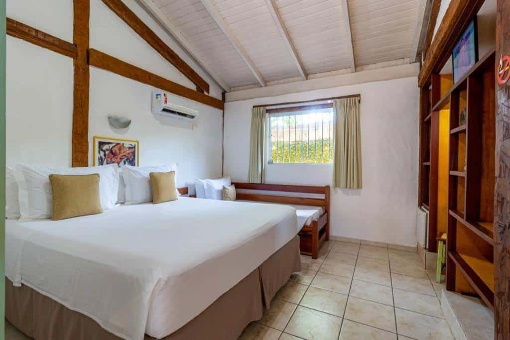 Quarto da Pousada Tambayba com uma cama de casal, uma de solteiro, um armário de conceito aberto com frigobar e televisão