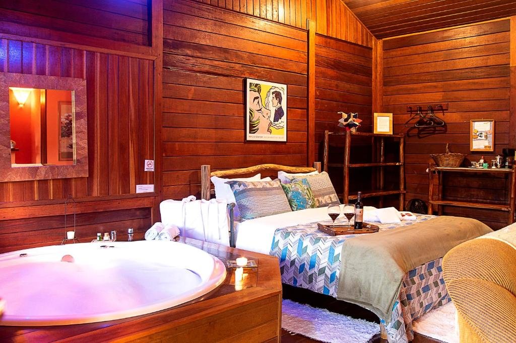 Quarto com paredes de madeira, cama de casal, quadro na parede e banheira ao lado da cama.