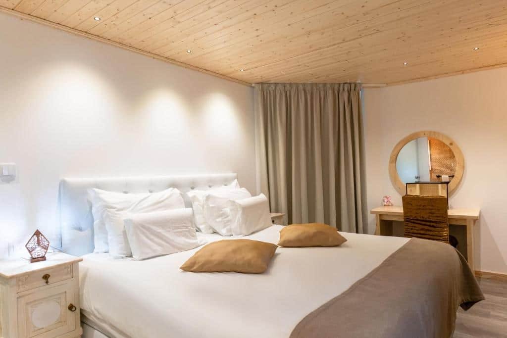 Quarto do Quinta da Barroca com cama de casal do lado esquerdo da imagem, com uma cômoda com luminária do lado direito da cama e do lado esquerdo da cama uma mesa de madeira com cadeira e um espelho redondo preso na parede.