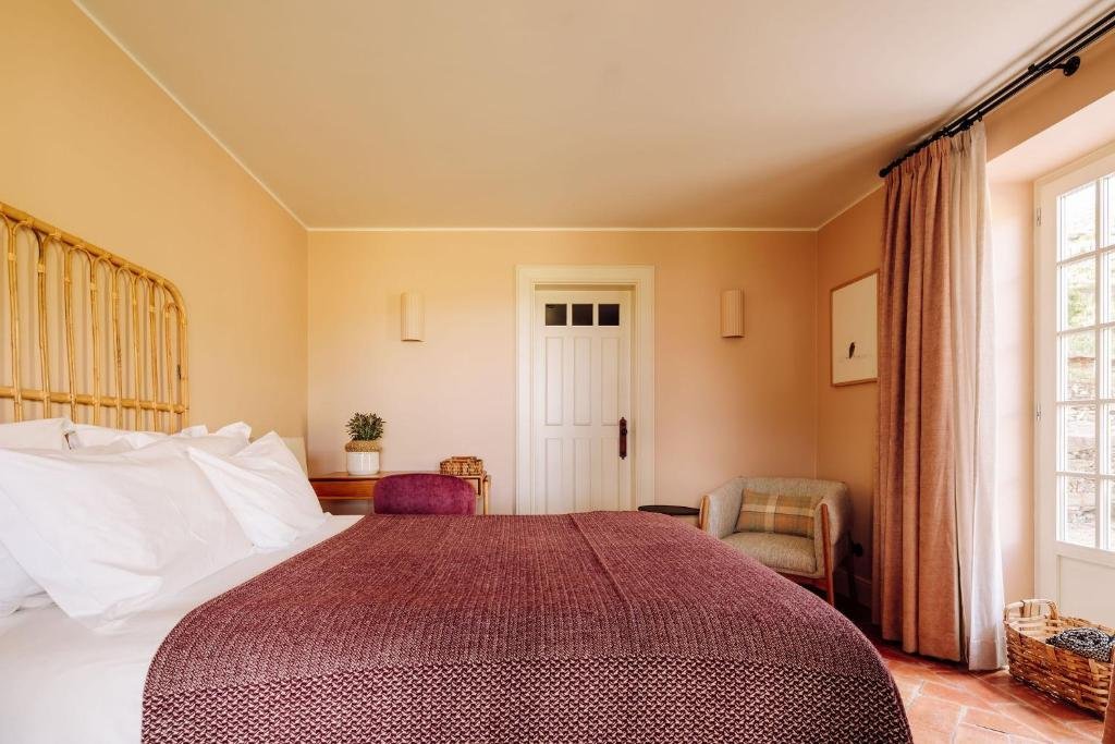 Quarto do Quinta Nova Winery House – Relais & Châteaux com cama de casal do lado esquerdo da imagem, do lado esquerdo da cama uma mesa de trabalho com cadeira e em frente a cama uma poltrona.