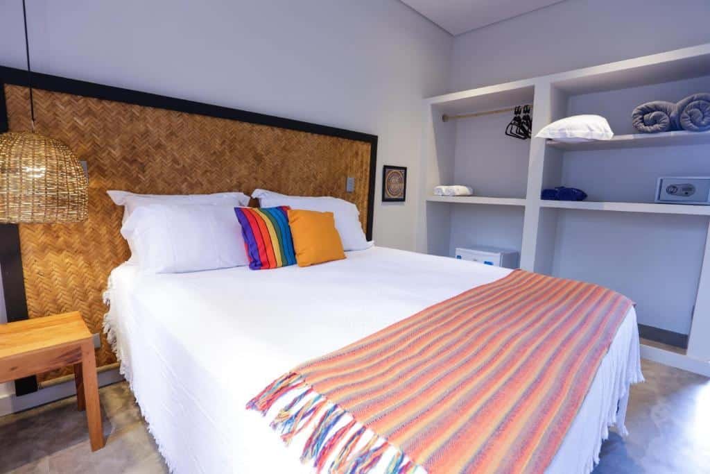 Quarto na Pousada TeMoana com um armário de conceito aberto com toalhas e edredons, uma cama de casal com almofadas e travesseiros, além de uma cabeceira rústica