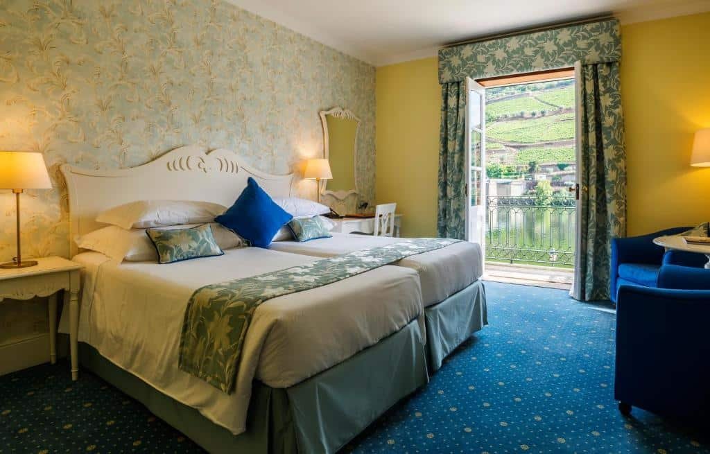 Quarto do The Vintage House – Douro com cama de casal do lado esquerdo da imagem, com uma cômoda em cada lado da cama com luminária, do lado esquerdo da cama uma mesa com cadeira e em frente a cama duas poltronas.
