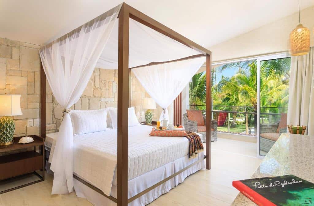 Quarto do The Westin Porto de Galinhas All-Inclusive com uma varanda com vista para o jardim e duas poltronas, há uma cama de casal com estilo bangalô com chão de madeira e alguns itens de decoração