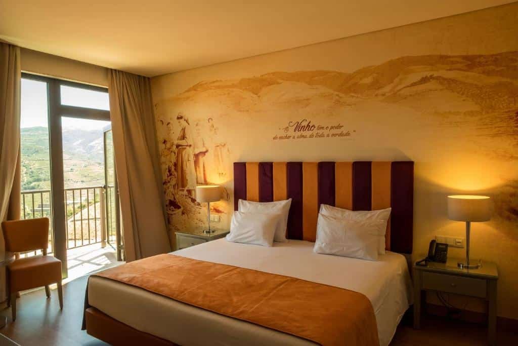 Quarto do Vila Gale Douro Vineyards com cama de casal do lado direito da imagem com uma cômoda em cada lado da cama com luminária. Representa hotéis no Vale do Douro.