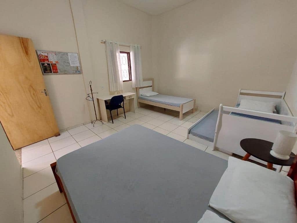 Foto do quarto em Recanto Serra Negra - Sossego e lazer!  A cama de casal está no canto inferior da foto, ao lado dela, na direita, há três camas para crianças. Do lado da cama no fundo à direita há uma mesa com cadeira. A porta do quarto está na esquerda, de frente para a cama de casal.
Ilustra o post sobre airbnb em Serra Negra.