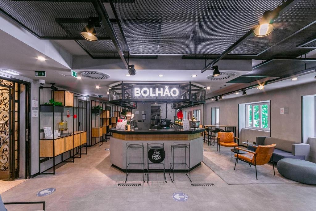 Sala de estar do ibis Porto Centro Mercado Bolhao com sofás e poltrona do lado direito da imagem, no centro um balcão com três cadeiras.