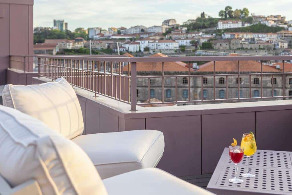 Sacada do Hotel das Virtudes durante o dia com duas poltronas do lado esquerdo uma mesa do lado direito com duas bebidas em cima e ao fundo vista do centro da cidade.