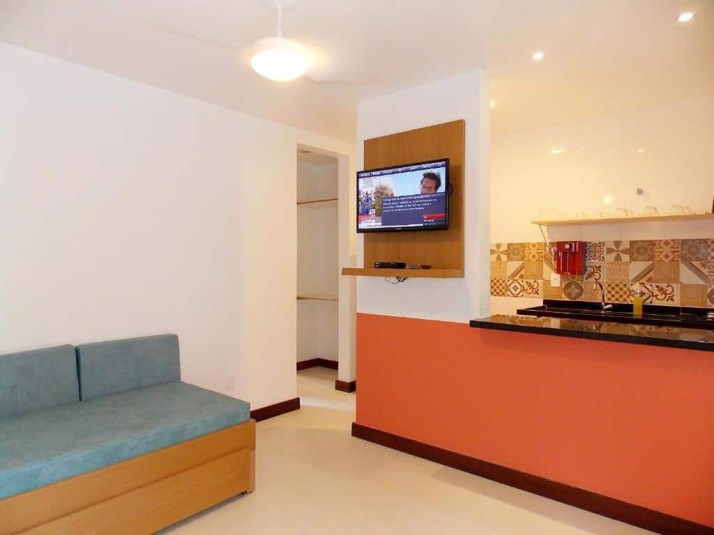Sala e cozinha do airbnb Ancoradouro Flats. No canto esquerdo há um sofá e no lado direito está a cozinha, onde há uma TV na parede e um balcão dividindo os cômodos.