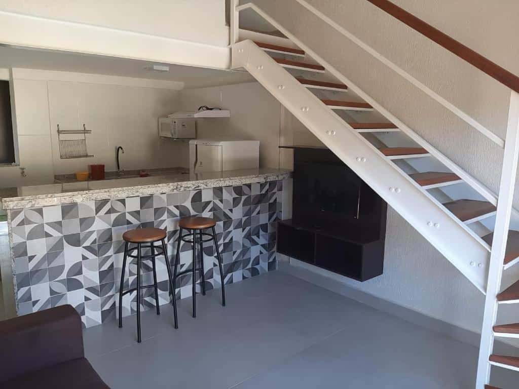 Sala e cozinha do airbnb Bugio Flats. No lado esquerdo está o sofá da sala, em sua frente há um pequeno hack com a TV e no fundo está a cozinha. No lado direito há uma escada que leva até o segundo andar. Imagem para ilustrar o post airbnb em Ilha Grande.