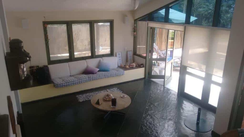Sala da Casa em Toque-Toque Pequeno, bem ampla, com janelas e porta de vidro, um pequeno sofá, uma mesinha redonda ao centro e algumas almofadas no sofá