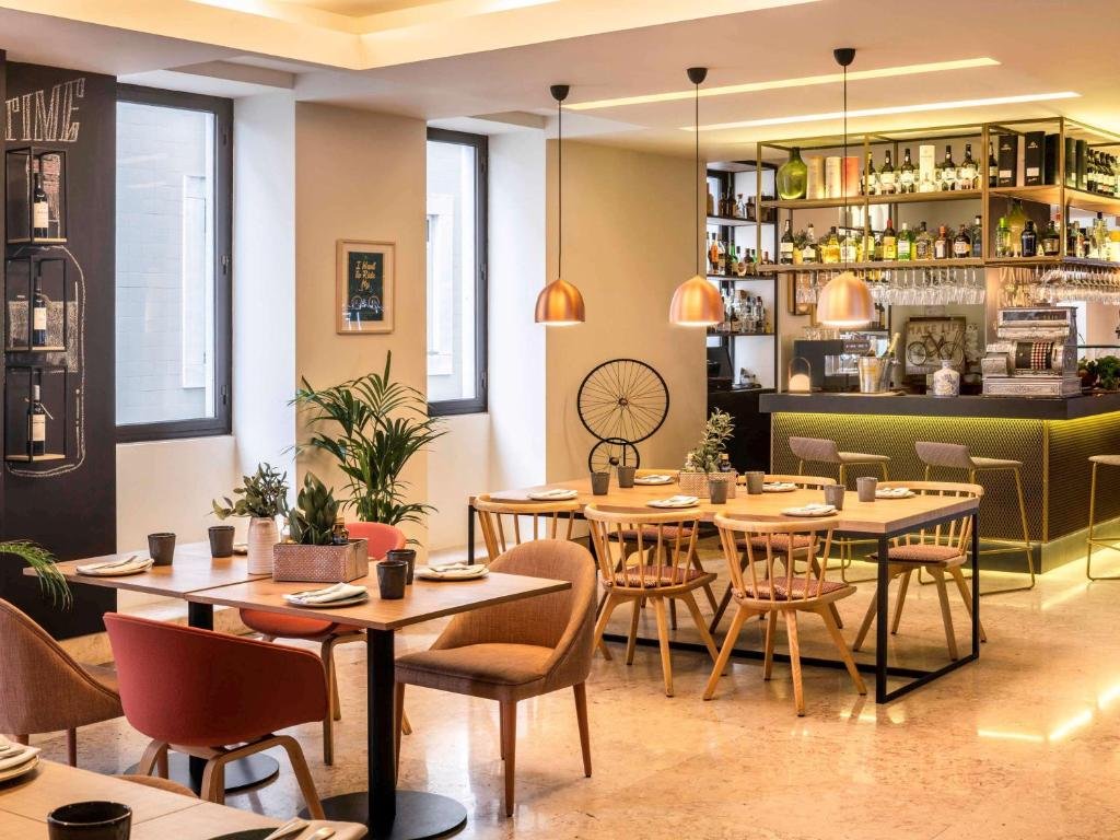 Sala de refeição do Mercure Porto Centro Santa Catarina com cadeiras e mesa a frente e ao fundo um balcão com bebidas.