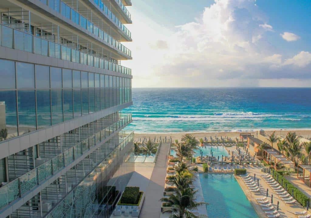 vista do mar pela janela do Secrets The Vine Cancun, mostrando a lateral do hotel, a piscina e a praia