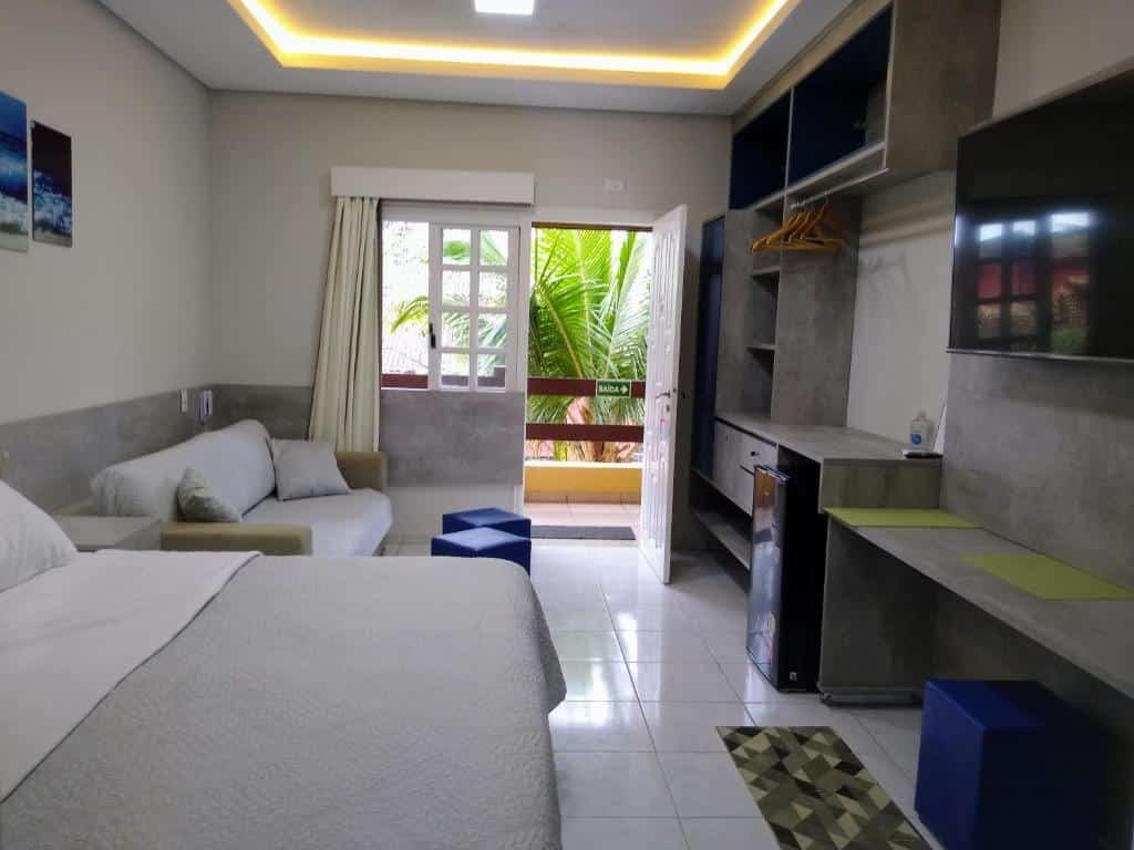 Cômodo completo do STUDIO A RIVIERA - Flat Service 318, com uma cama de casal, um pequeno sofá, uma varanda, um armário de conceito aberto, um frigobar e uma televisão, para representar pousadas em Riviera de São Lourenço