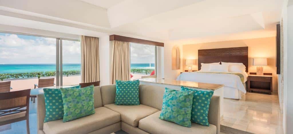 suíte com cama de casal e uma sala em em frente a cama, além de uma saca privativa na lateral com vista para o mar no Grand Fiesta Americana Coral Beach Cancun