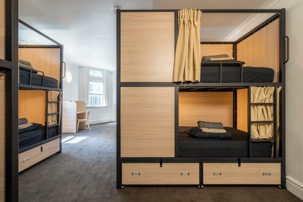 Quarto do Tequila Sunrise Hostel Sydney. Uma cama beliche do lado direito, com gavetas e cortinas. Do lado esquerdo uma beliche semelhante. No fundo uma mesa de trabalho e janelas.