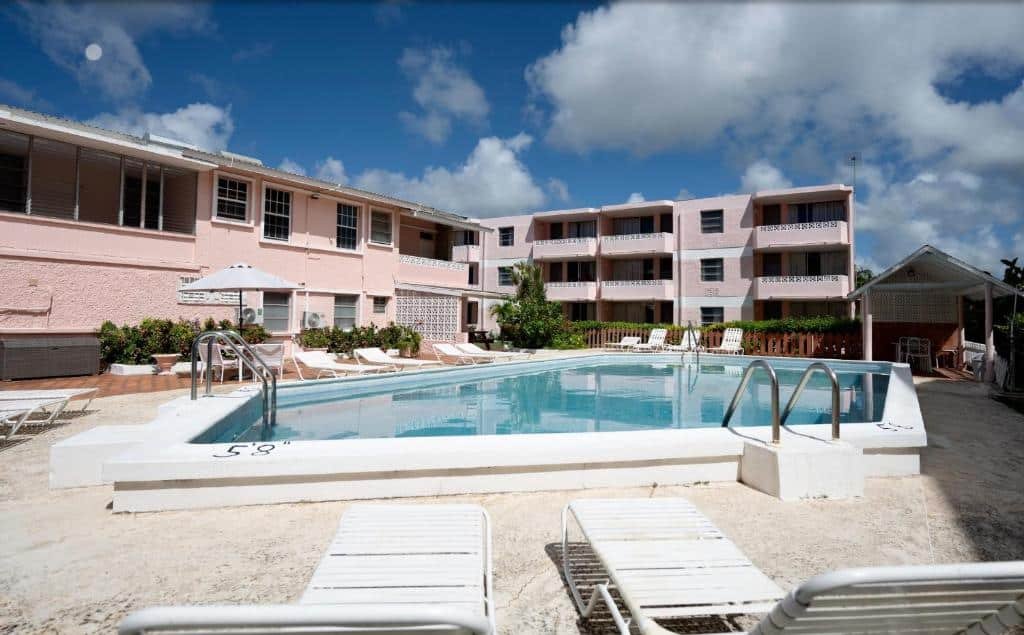Área externa do The Monteray Hotel com uma piscina ao ar livre no centro e ao redor cadeiras de tomar sol, no fundo o hotel. Imagem ilustrando post Hotéis em Barbados.