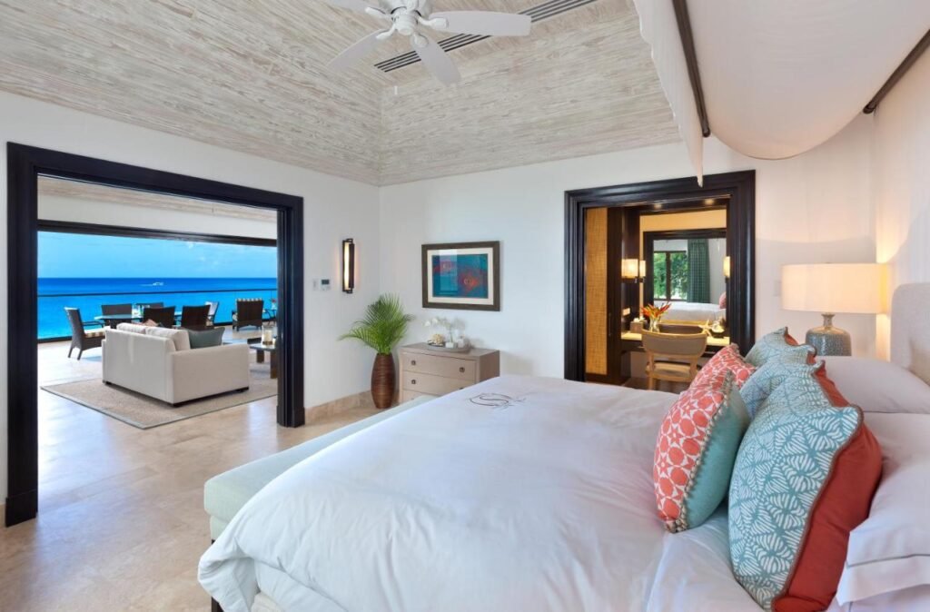 Quarto do The Sandpiper. Uma cama de casal do lado direito, no fundo um abajur e uma penteadeira. Do lado esquerdo a porta do quarto ocm vista para a varanda.