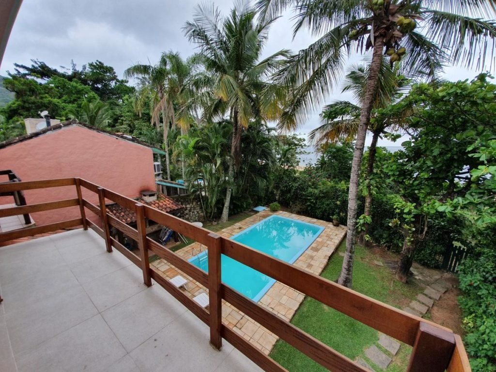 Visão da sacada da Casa pé na areia em Toque Toque com vista para a piscina, o jardim e a entrada do local, logo após as árvores já é possível ver o mar