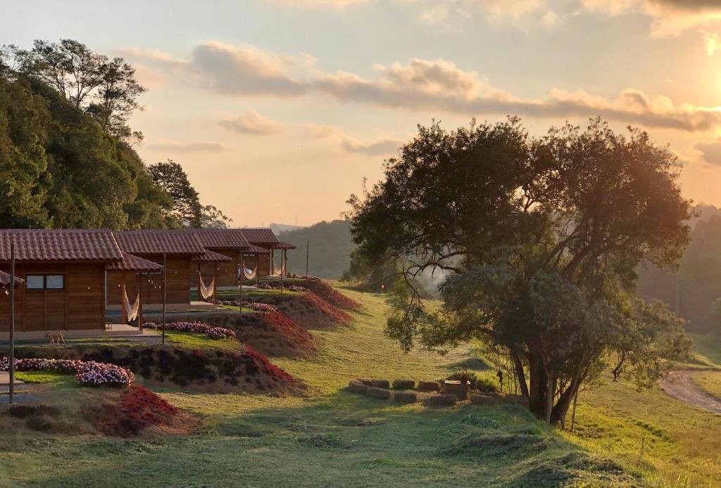 chalés com parede de madeira, rede na varanda e jardins à frente, com bastante natureza à frente e pôr do sol