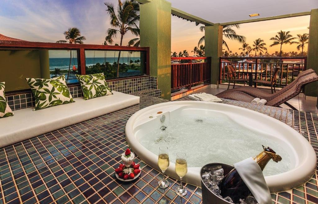 Sacada do Vivá Porto de Galinhas Resort com uma banheira de hidromassagem, com taças de champanhe e morangos, para representar resorts em Muro Alto