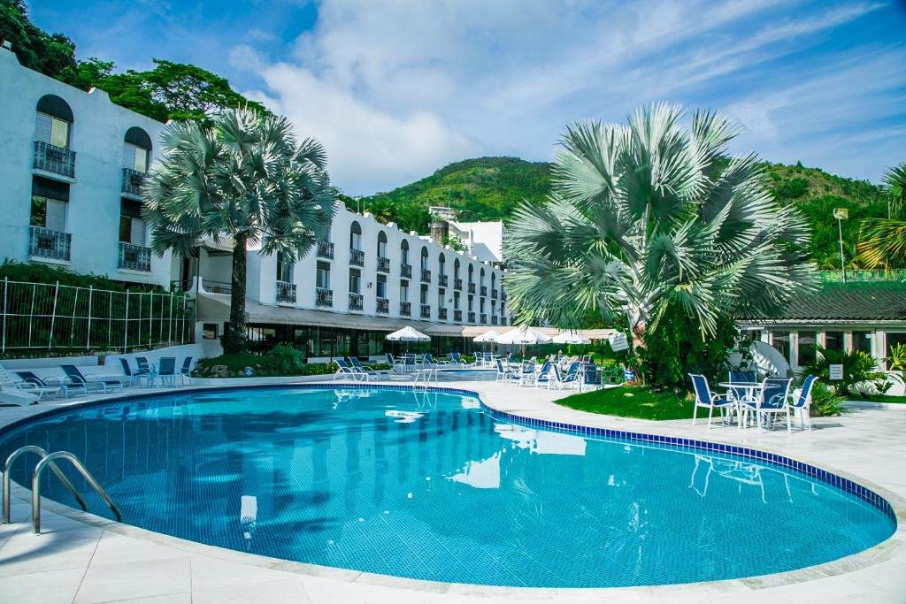 Piscina no Wembley Inn Hotel com deck amplo ao redor com cadeiras e mesas, além de árvores e gramados, para representar resorts em Ubatuba